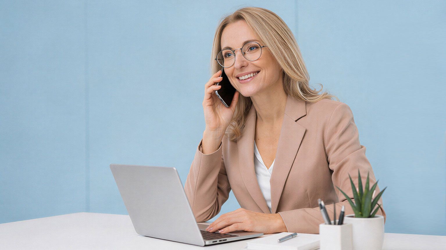 Az ECK-hoz való csatlakozás könnyedségét érzékeltető kép. A képen egy szőke hölgy látható irodai környezetben, egy íróasztalnál, egy laptop előtt ülve. A hölgy visszatérő szereplője az oldalnak, az ECK alkalmazás felhasználóját jelképezi. Ezen a képen kedves mosollyal telefonál, éppen az ECK ügyfélszolgálatával beszél, akik segítenek neki a csatlakozási folyamatban. A kép üzenete, hogy az ECK szolgáltatáshoz való csatlakozás egyszerű és stresszmentes folyamat